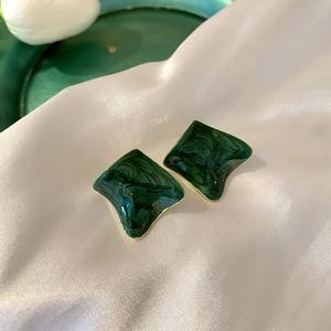 Macro detail of irregular green enamel earrings with gold edges on white silk cloth