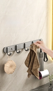 Detail of grey wall-mounted 5-hook rack holding a bath ball, towel, and hair dryer