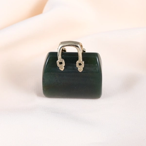 Macro view of a dark green gemstone mini handbag pendant with a golden metal handle