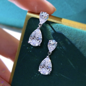 Macro shot of silver teardrop earrings with sparkling crystals on dark green velvet