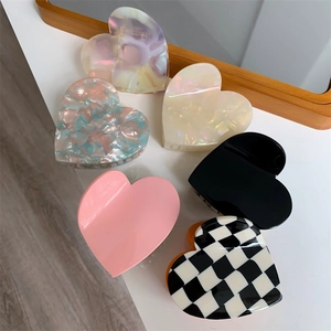 Colorful heart-shaped hair claw clips in various patterns on a clean white desk surface