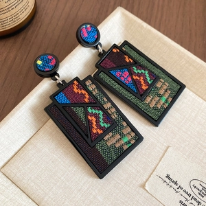 Detail view of rectangular geometric earrings with colorful woven embroidery patterns