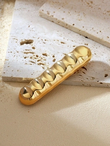 Detail of a wavy gold bubble-textured hair clip on elegant beige travertine stones