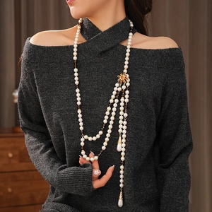 Detailed view of layered pearl necklace with golden pendants on grey knitwear garment