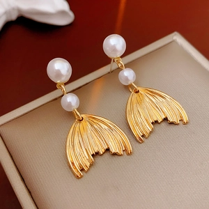 Detailed view of golden fishtail earrings with elegant white gradient pearls on beige box