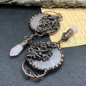 Close-up of vintage bronze dragon earrings with rose quartz stone and crystal pendant