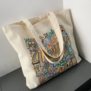 Detail of colorful embroidery on off-white canvas tote bag featuring camera and palm tree