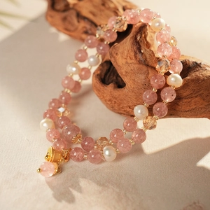Close-up of double-layer pink strawberry quartz and pearl bracelet on a dark wood stand