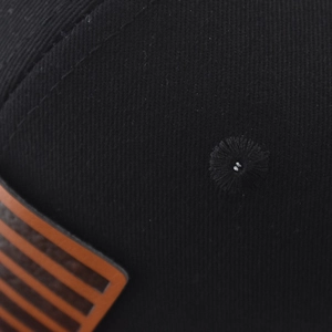 Dettaglio cappello nero con occhiello ricamato e etichetta in pelle marrone goffrata