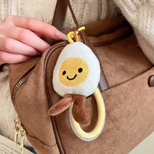 Plush poached egg doll pendant with smiling face and legs hanging on a brown bag