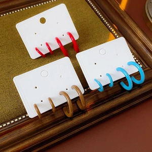 Detailed view of colorful C-shaped resin earrings in red blue and brown on a wooden tray
