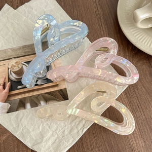 Three large heart-shaped hair claws in iridescent blue, pink and clear on a wooden tray