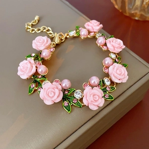Détail de roses en résine rose, feuilles vertes et perles sur un collier floral doré