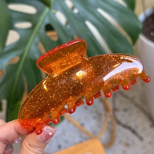 Detail of amber acrylic shark hair claw clip with golden glitter and seven teeth design