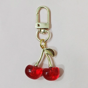 Close-up of red resin cherry keychain with golden metal leaves and a D-ring clasp