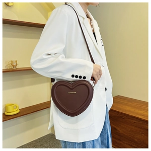Détail d'un sac bandoulière marron foncé en forme de cœur avec texture cuir délicate