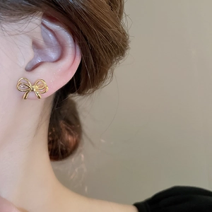 Macro view of gold bow stud earring with mirror finish on model's ear