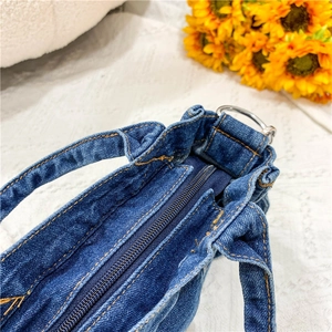 Detailed close-up of blue denim bag with orange stitching, metal D-ring and zip closure