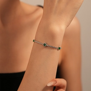 Close-up of silver tennis bracelet featuring green emerald zircons on a model's wrist