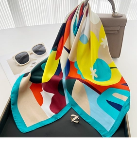 Detail of multi-color printed silk scarf draped on a handbag with fashion accessories