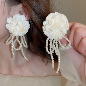 Detail of white fabric flower earrings with faux pearl tassels on model's ear