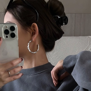 Close-up of model wearing silver geometric hoop earrings with irregular liquid metal texture
