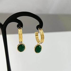 Close-up of gold hoop earrings featuring round green aventurine stones on a black stand