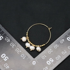 Elegant gold hoop earrings with white teardrop pearls and gold beads on a black background
