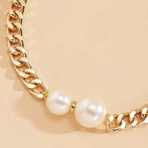 Chunky gold chain necklace featuring two large white pearls on a minimalist warm background