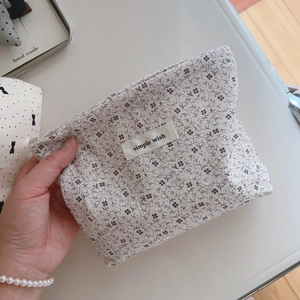 Detail showing hand holding small floral cotton cosmetic bag with simple wish label