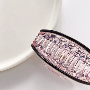 Close-up of pink oval hair claw clip with black trim and clear texture on white surface
