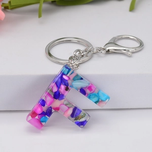 Detail of resin letter F keychain with colorful blue and pink fragments and silver clasp