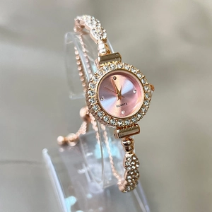 Close-up of rose gold quartz watch with pink dial and rhinestone bezel on stand