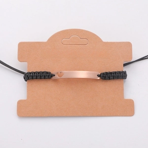Detail of hand-woven black rope bracelet with rose gold hollow heart bar on card
