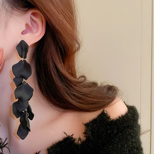 Detail view of long black fringe earrings with matte petals on a model's ear
