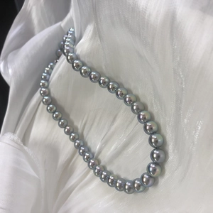 Macro detail of round Akoya-style pearls on white silk showing deep metallic luster