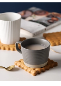 Detail of cookie-shaped black walnut wood coaster with matte ceramic coffee cups
