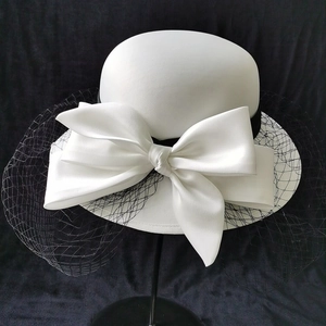 Elegant white bridal fascinator hat with satin bow and black mesh veil on dark background