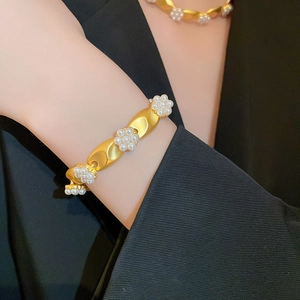 Detailed view of matte gold floral bracelet with pearls styled on a black blazer