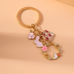 Golden keychain with pink rabbit, white cat floral wreath, and colorful enamel charms