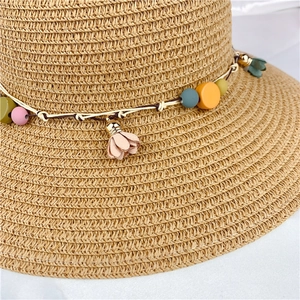 Close-up of woven straw hat featuring colorful beads and soft pink floral charms