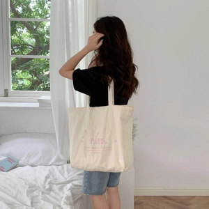 Woman wearing large beige canvas tote bag with pink Paris embroidery in a bright room