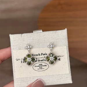 Close-up of four-leaf clover earrings with green stones, pearls, and zircons on linen card