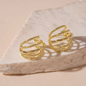 Detailed view of gold multi-layer spiral earrings with hammered metal texture on stone