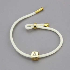 Detail eines weißen geflochtenen Armbands mit goldenem Strass-Buchstaben A Schieber
