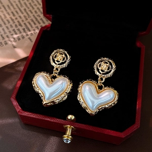 Golden heart-shaped pearl earrings in a red gift box with intricate clover patterns