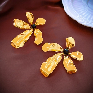 Close-up of golden flower earrings with irregular petals and a black bead center