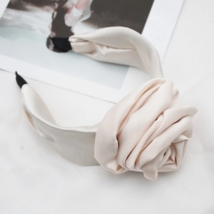 Close-up of a beige satin padded headband featuring a large fabric rose with silk texture