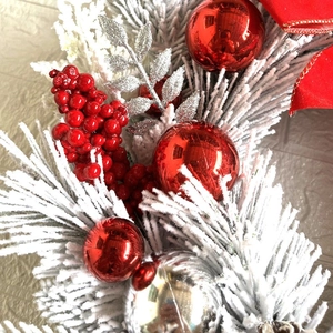 Detail of flocked Christmas garland with red berries, silver ornaments, and a festive bow