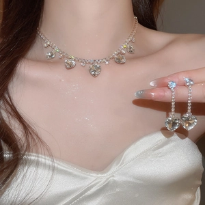 Detailed close-up of a silver zircon heart necklace and tassel earring set worn by a model